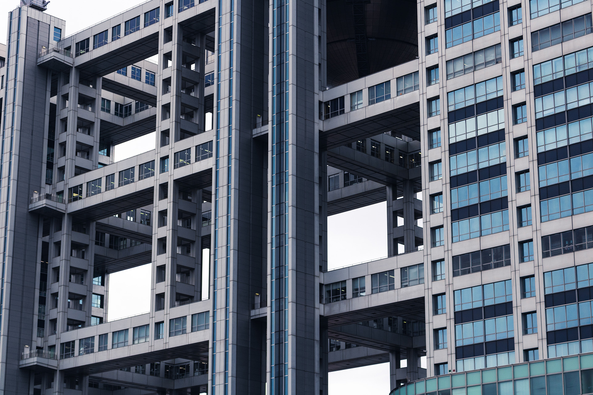 Modern concrete building made up of vertical and horizontal pillars with windows and large gaps between them.